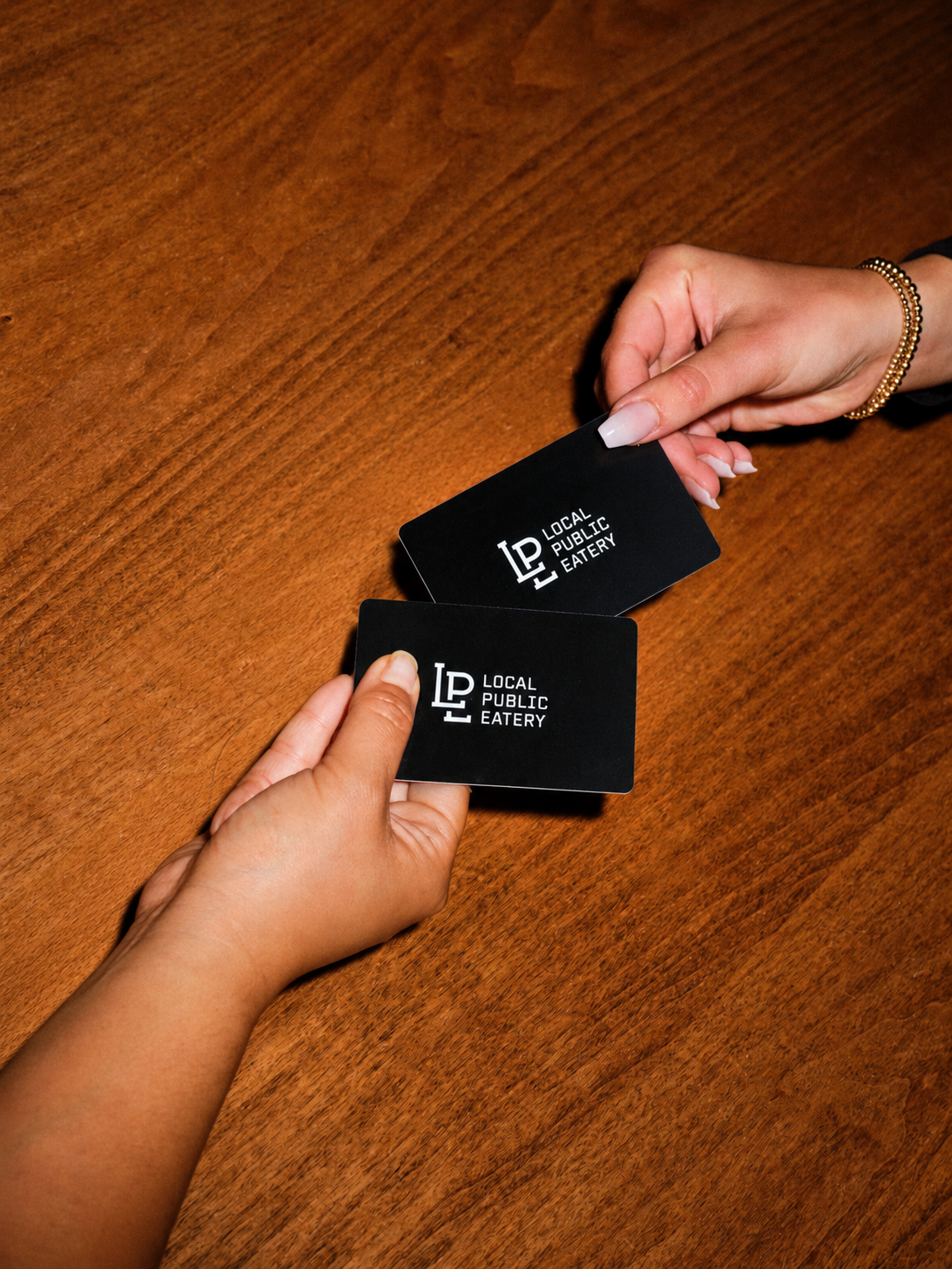 Hands exchanging Local Public Eatery Gift Cards over a table
